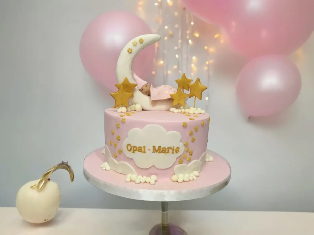 Welcome Baby Girl Cake by Harebell Creations Pink baby shower cake with moon, stars, clouds and sleeping baby topper, created by Harebell Creations.